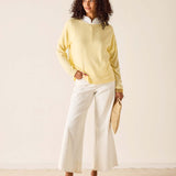 Woman wearing a light yellow sweater and white pants against a plain background