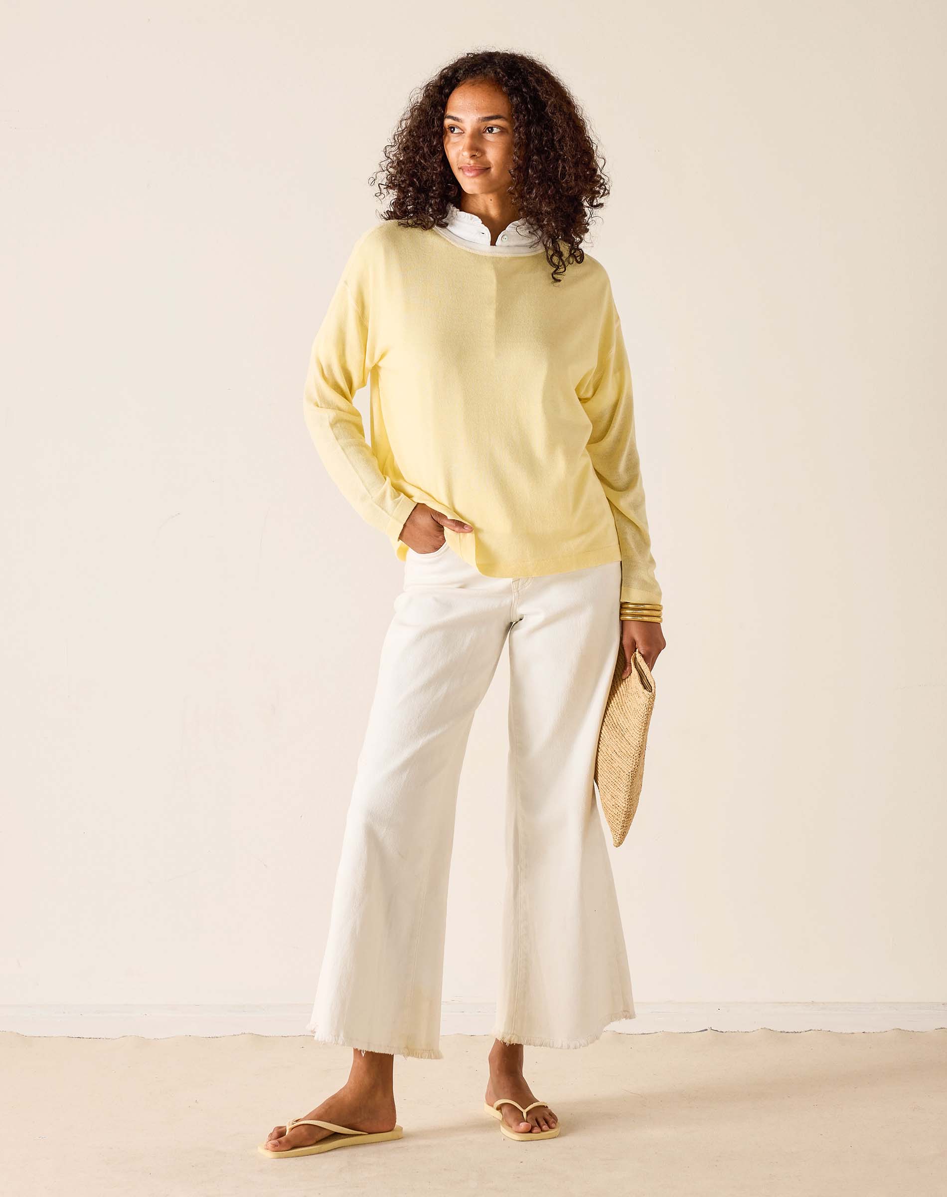 Woman wearing a light yellow sweater and white pants against a plain background