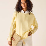 Woman wearing a light yellow sweater holding a woven bag against a beige background