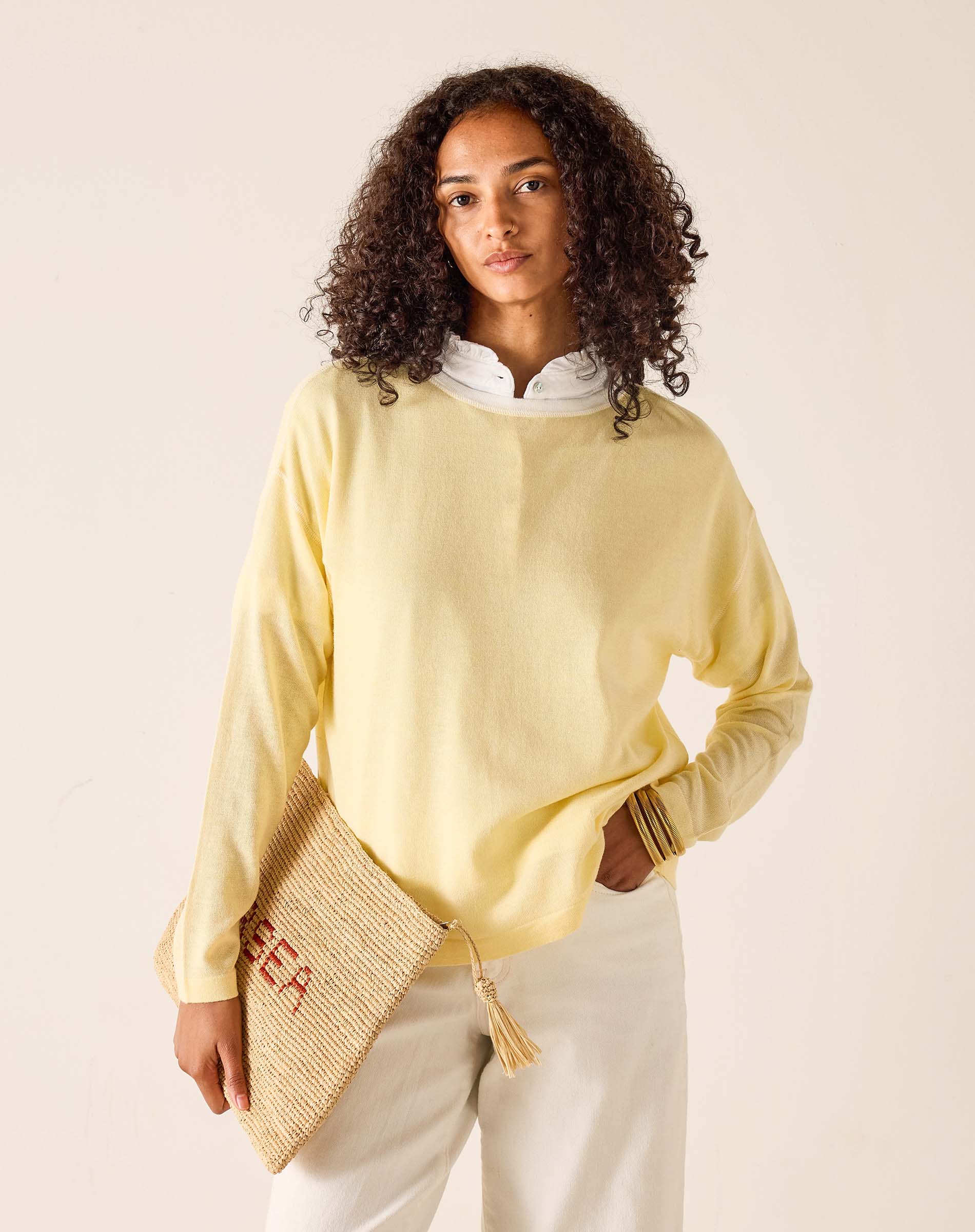 Woman wearing a light yellow sweater holding a woven bag against a beige background