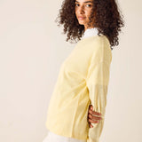 Woman wearing a light yellow sweater over a white shirt against a beige background