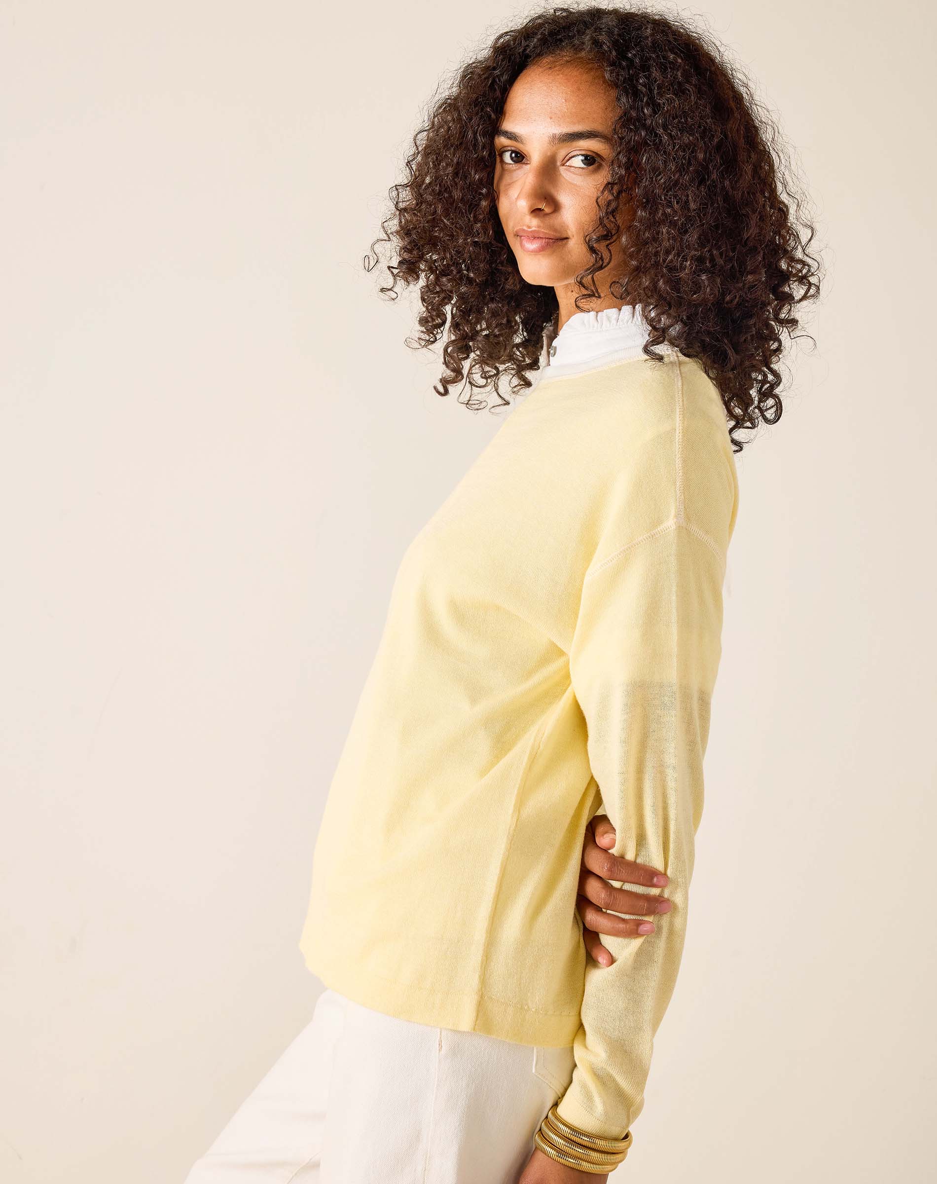 Woman wearing a light yellow sweater over a white shirt against a beige background