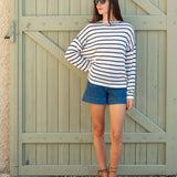 Woman wearing a striped sweater and blue shorts standing in front of a wooden gate.