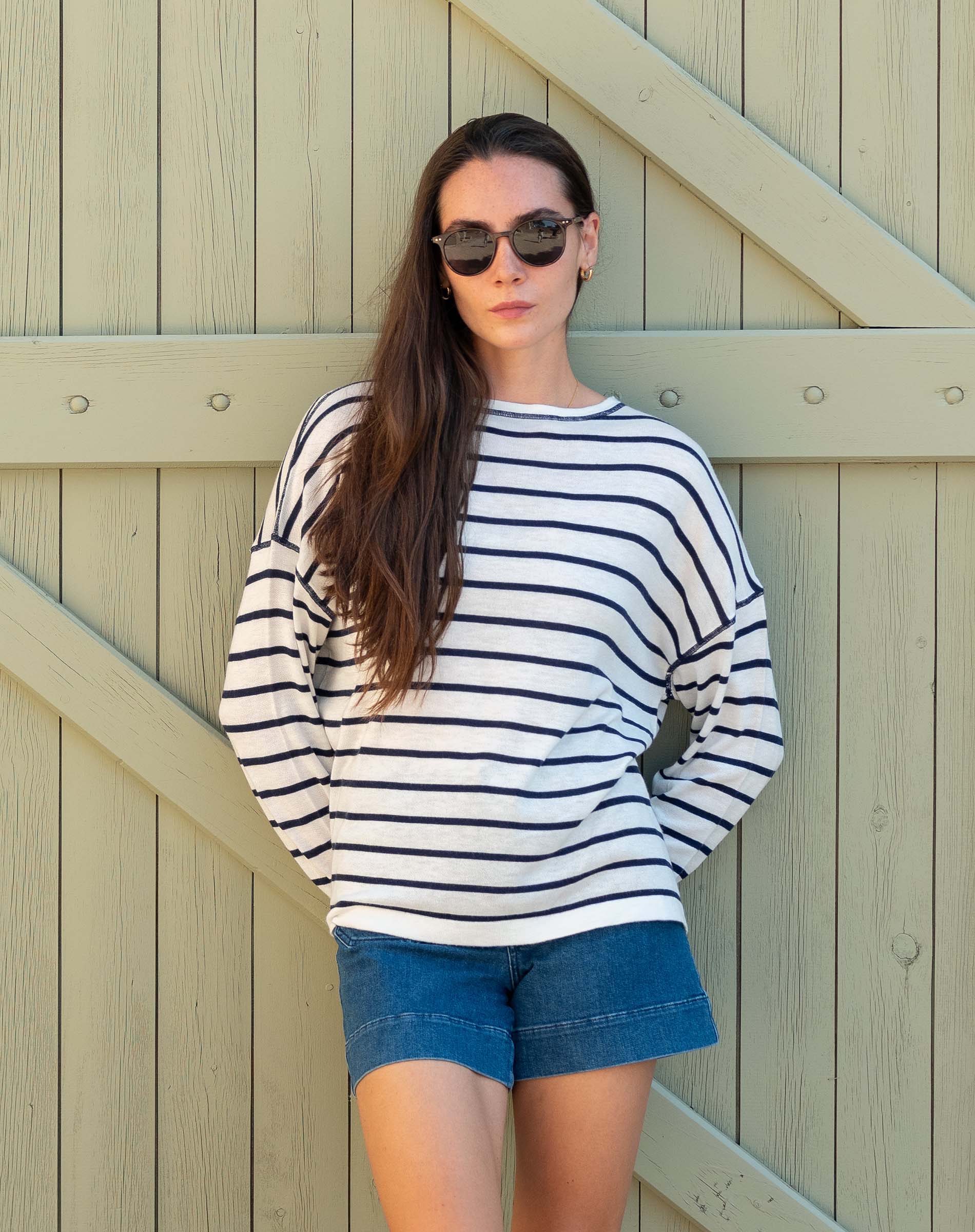 Woman wearing a striped sweater and denim shorts against a wooden background