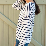 Woman wearing a striped long-sleeve shirt and denim shorts against a wooden fence.