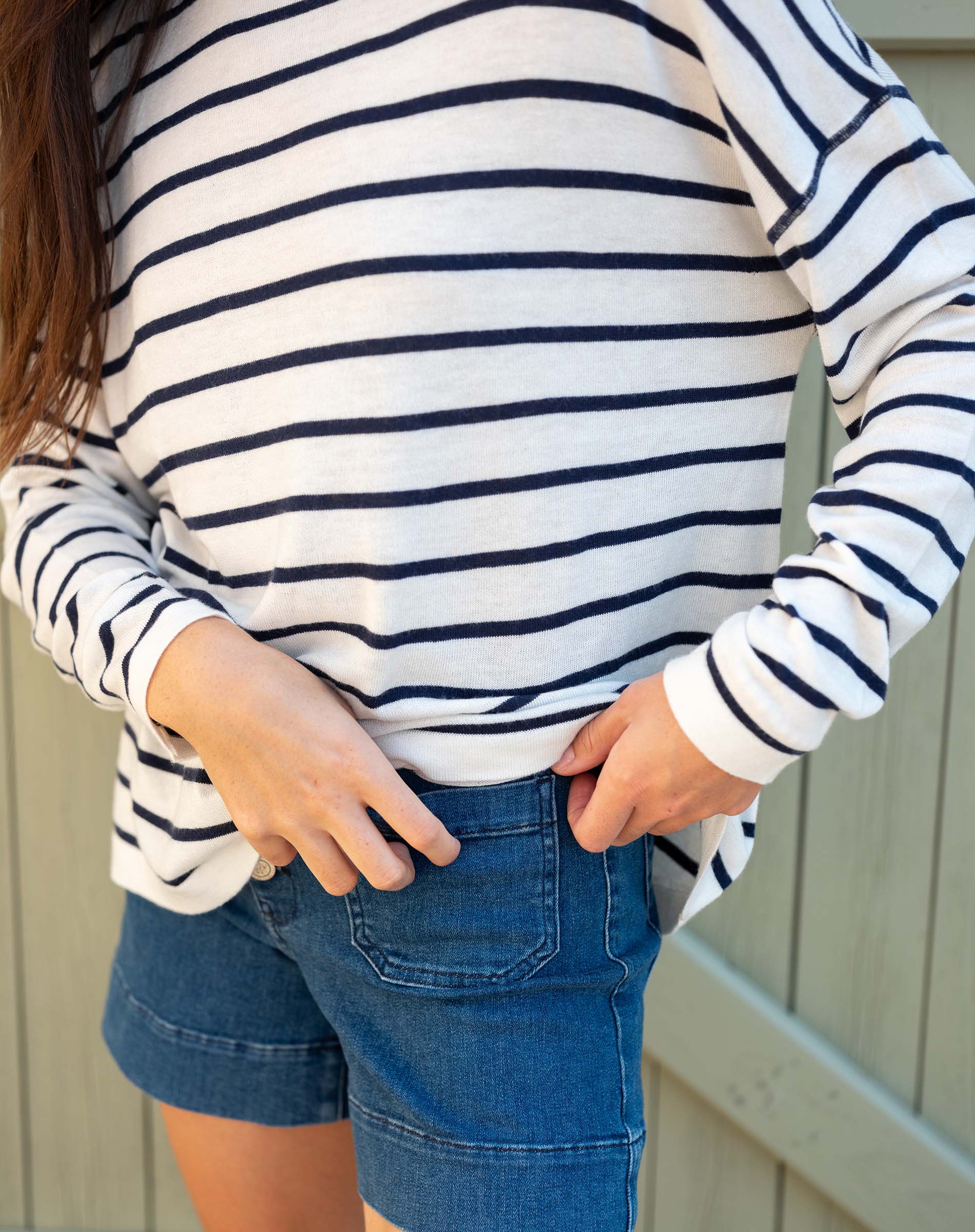 Person wearing a white and navy striped shirt with blue shorts against a neutral background