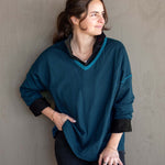Woman wearing a teal sweater with black cuffs and collar against a gray wall.