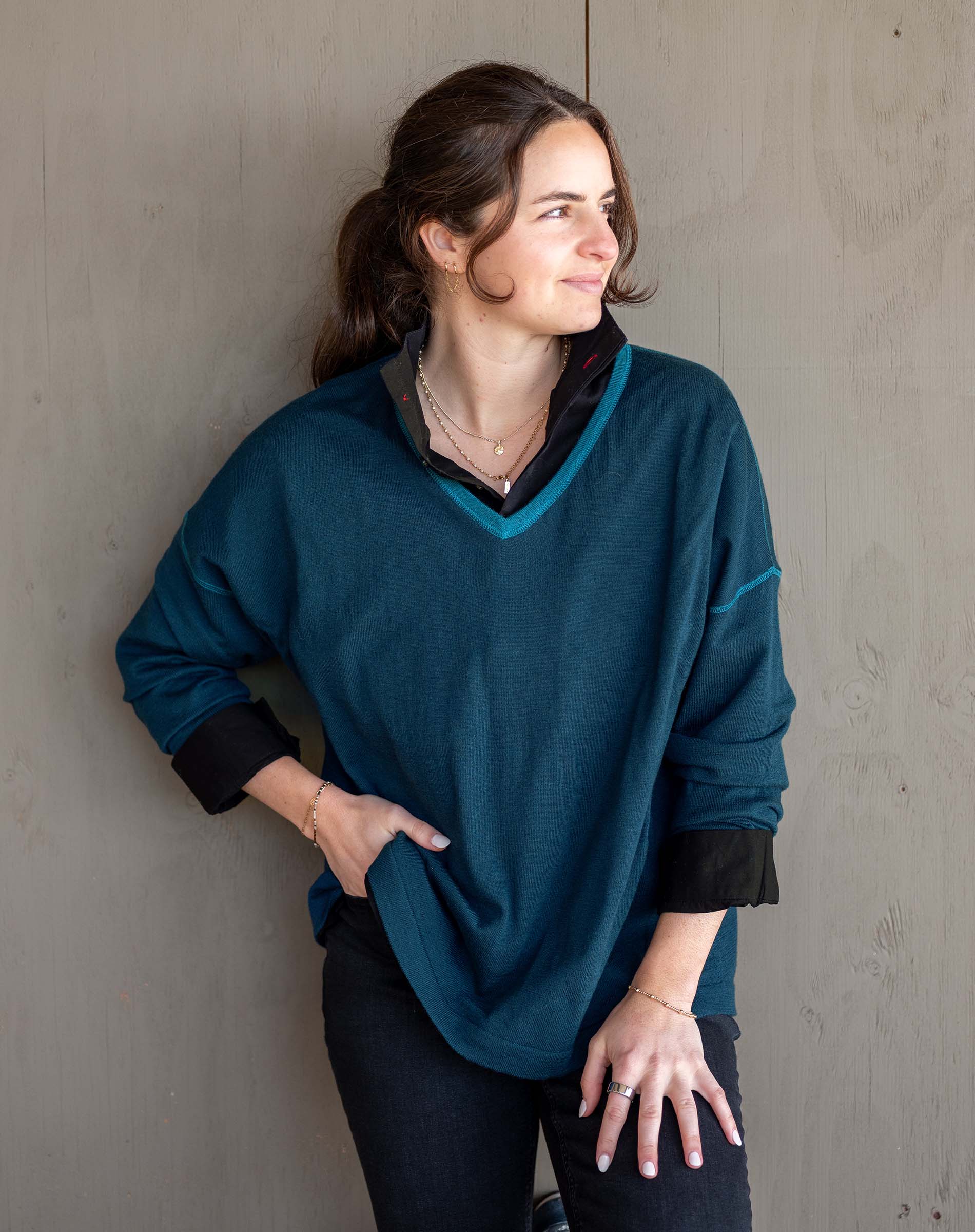 Woman wearing a teal sweater with black cuffs and collar against a gray wall.