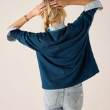 Back view of the deep teal V-neck knit top with puffed sleeves and light wash denim jeans.