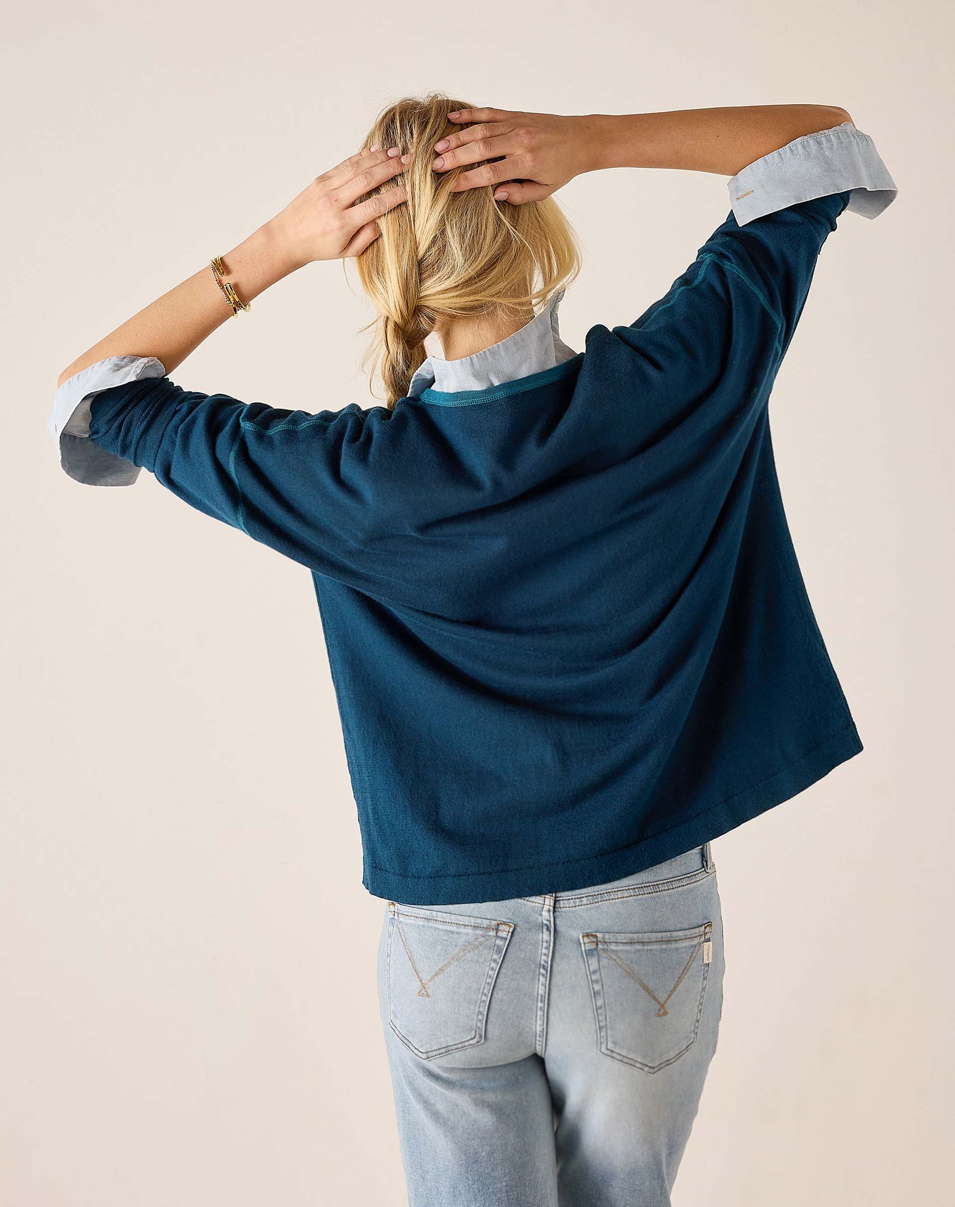 Back view of the deep teal V-neck knit top with puffed sleeves and light wash denim jeans.