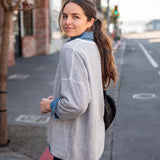 Woman standing on a street, wearing a light gray jacket and dark pants.