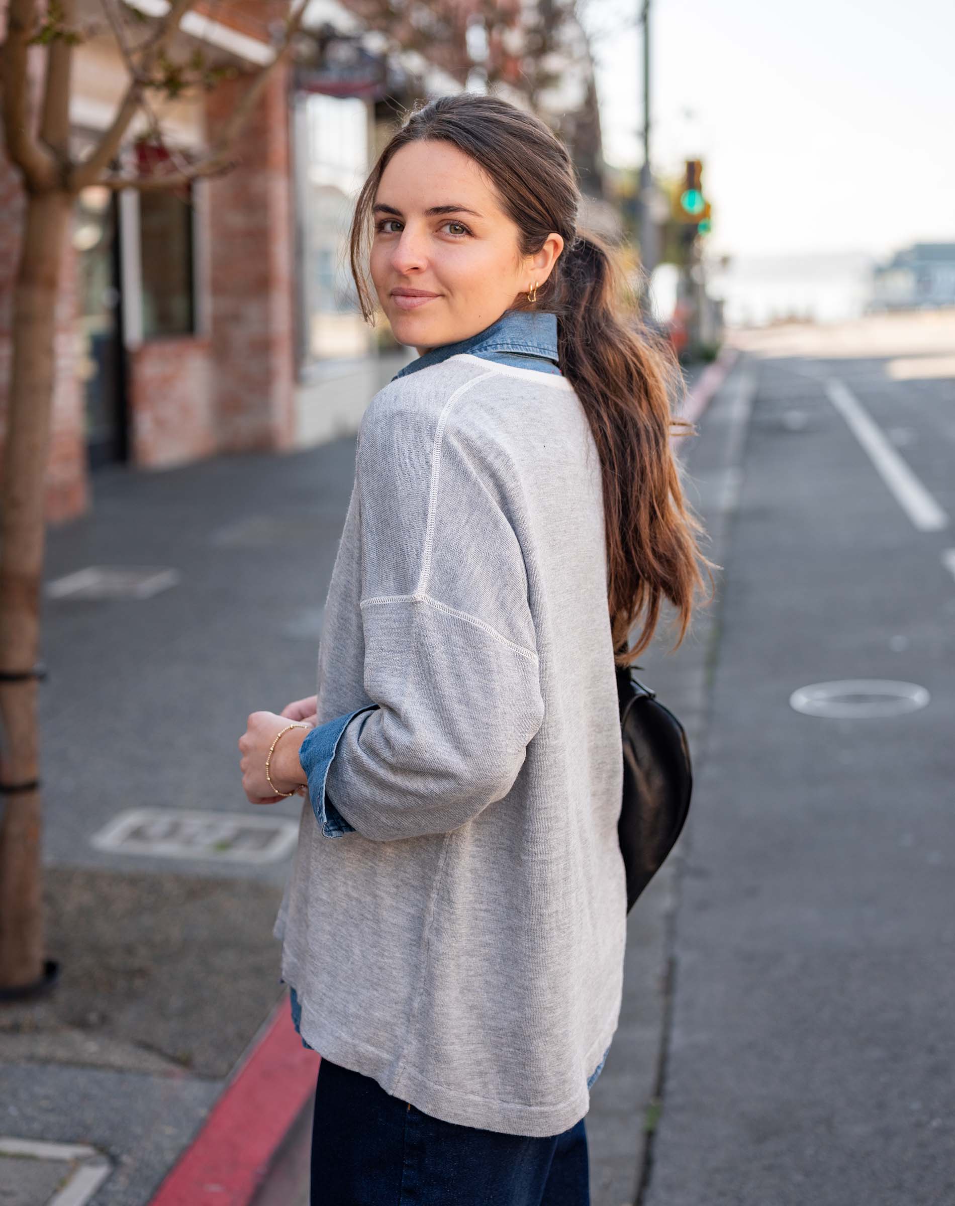 Woman standing on a street, wearing a light gray jacket and dark pants.