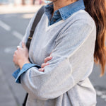 Woman wearing a light gray sweater over a denim shirt with a blurred street background