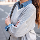 Woman wearing a light gray sweater over a denim shirt with a blurred street background