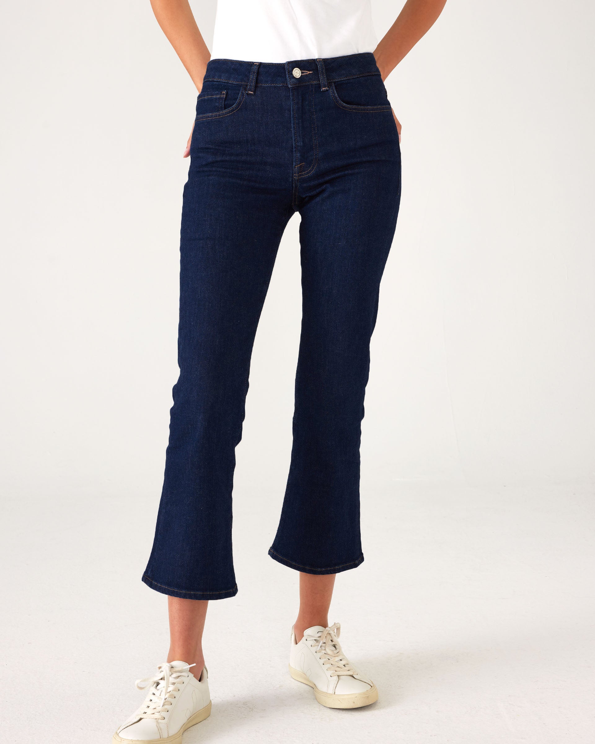 lower body of Woman showcasing Mersea moody blue Nomad cropped mini boot-cut jeans against white background