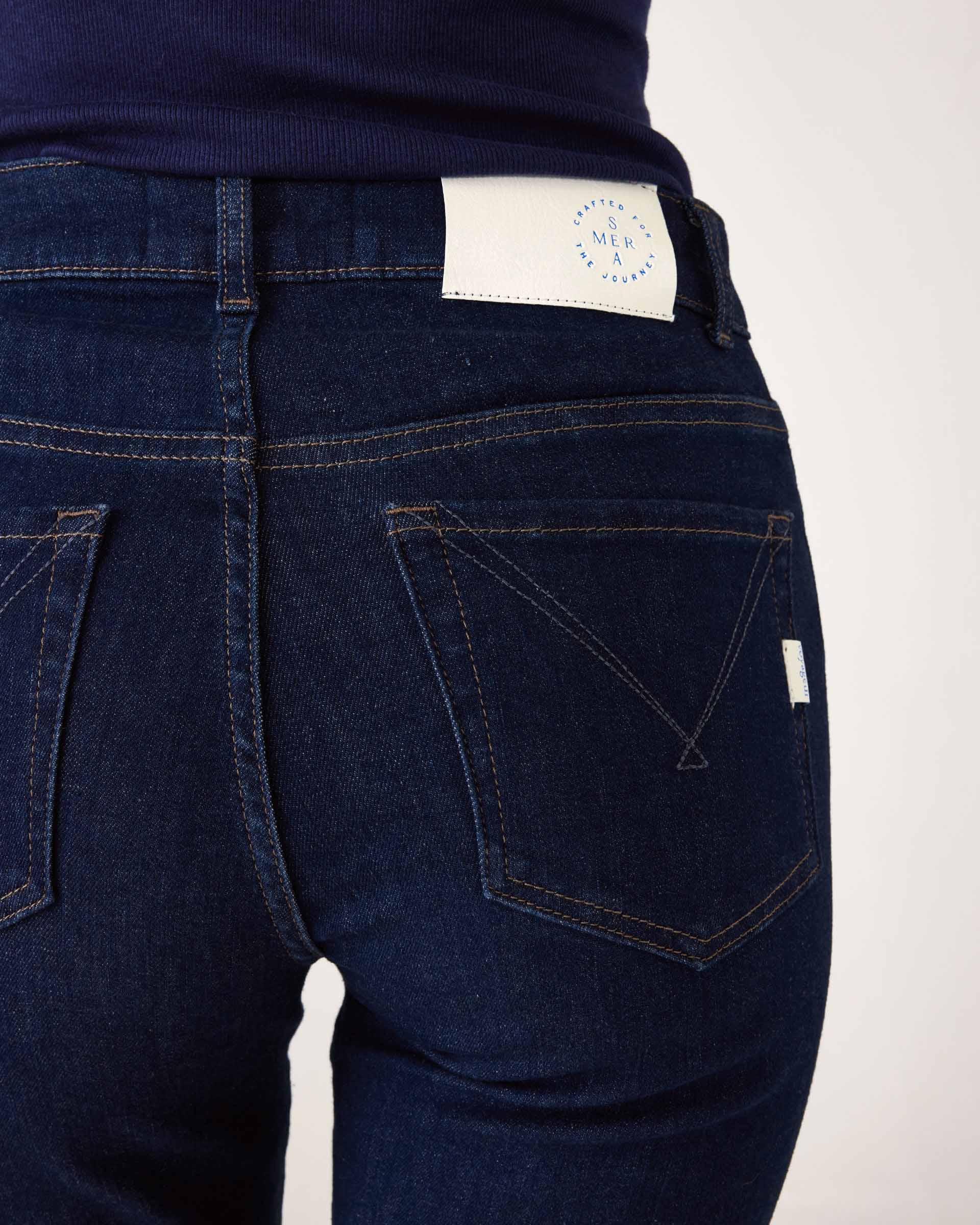 closeup rear view of Woman wearing Mersea Moody blue Nomad cropped mini boot-cut jeans standing against white background
