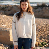 Cream knit sweater with whipstitch detailing on the sleeves and a small golden button at the neckline.