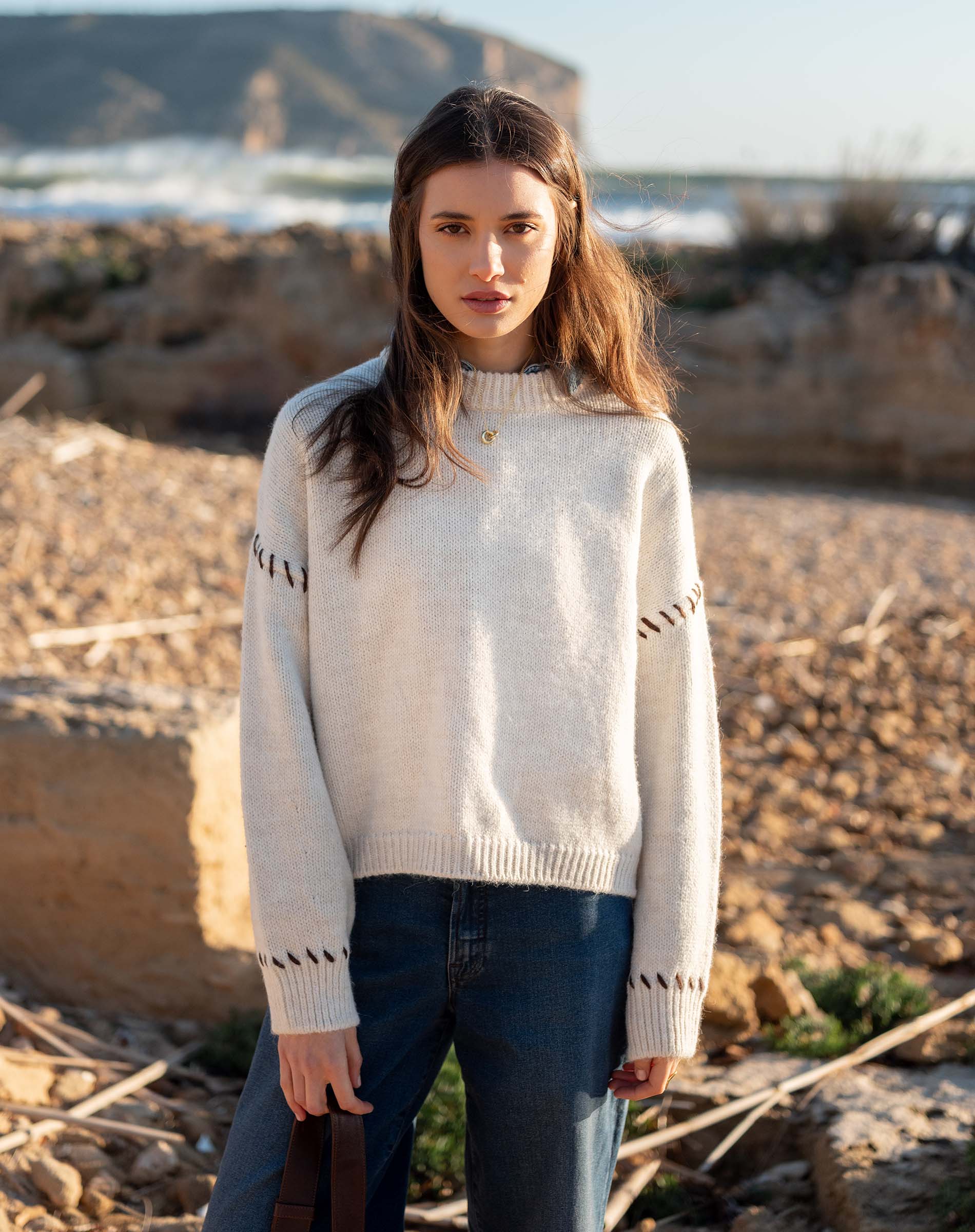 Cream knit sweater with whipstitch detailing on the sleeves and a small golden button at the neckline.