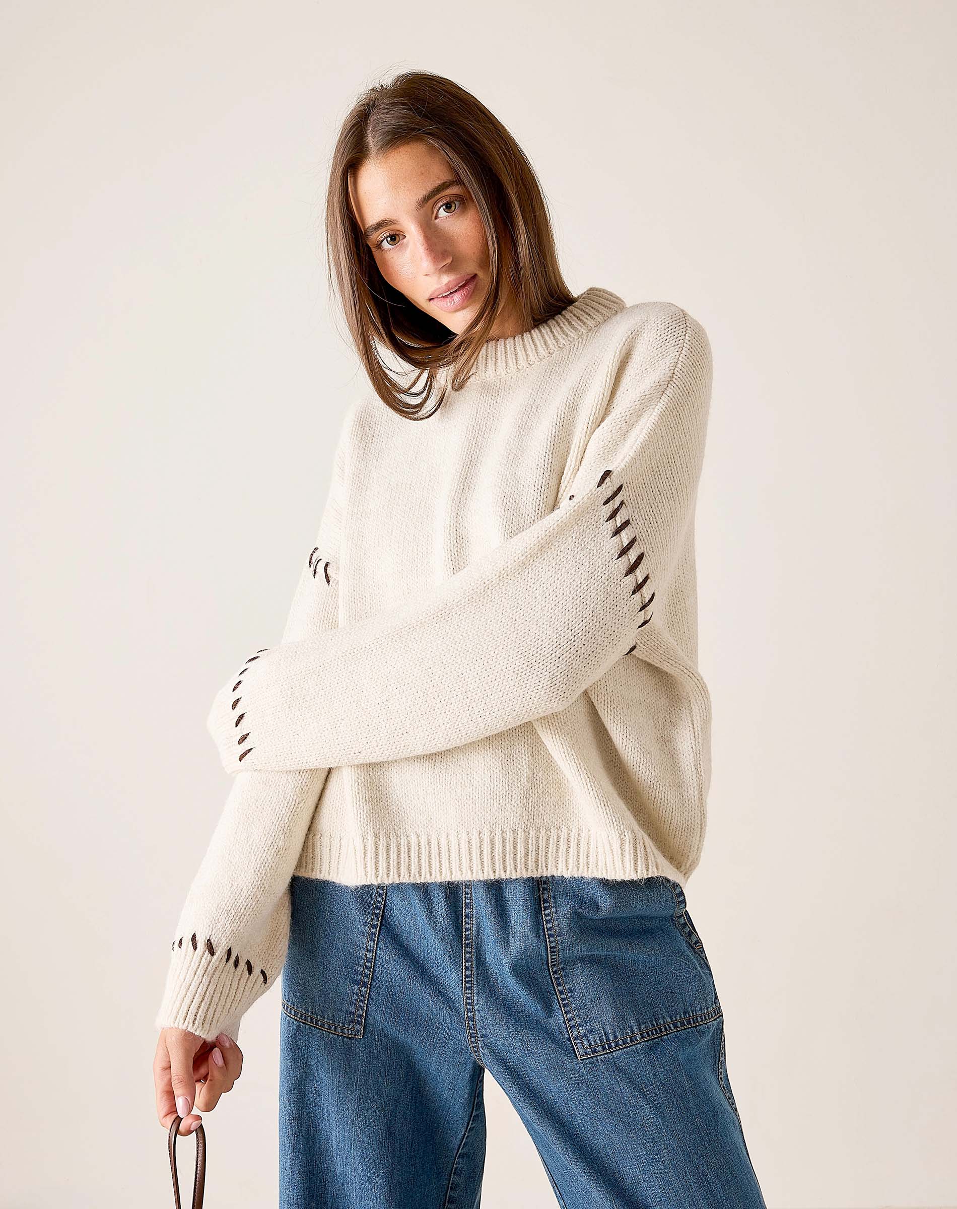 Cream knit whipstitch sweater with textured weave and statement stitching on the sleeves.