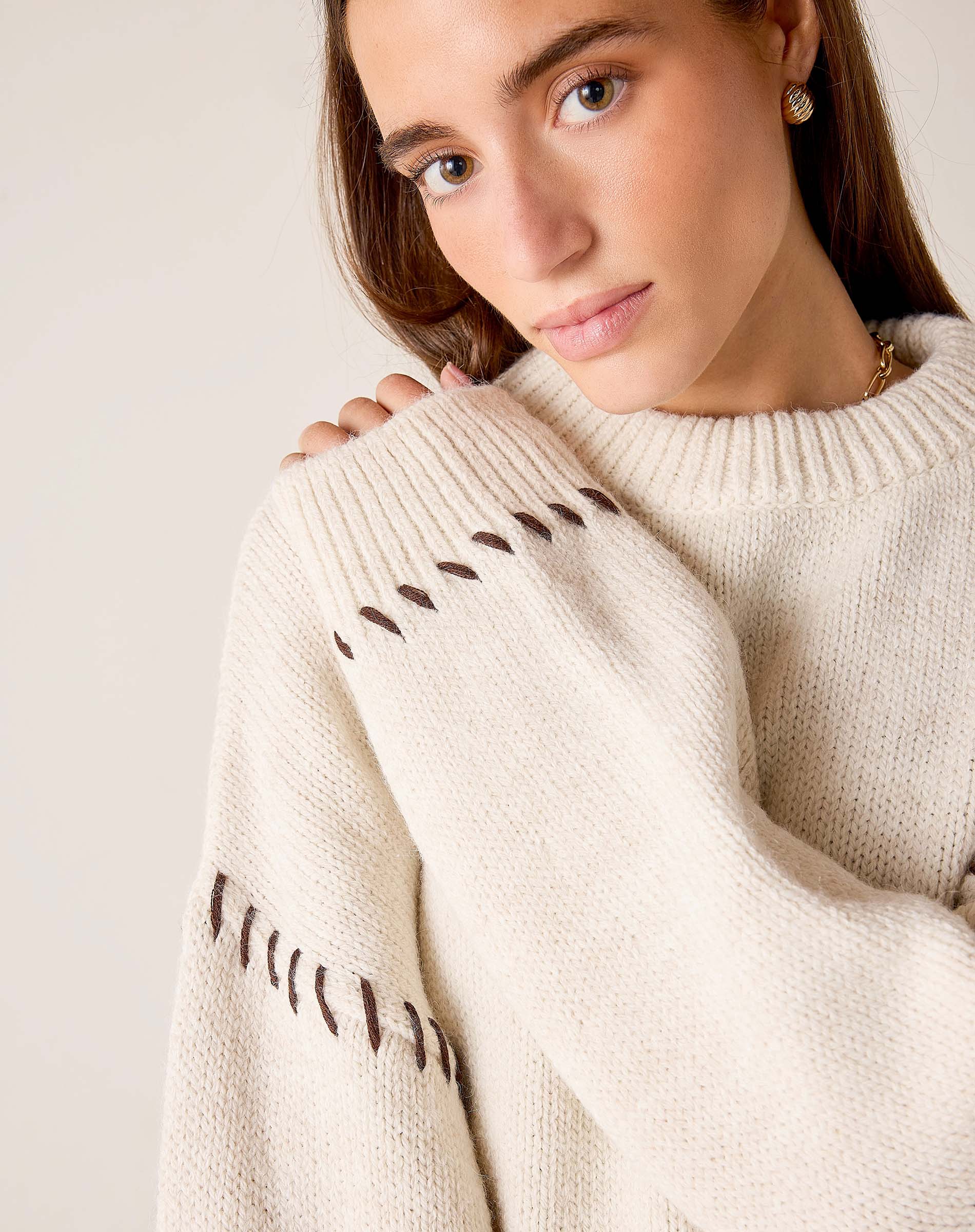 Cream knit sweater with whipstitch detail on the sleeves.