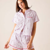 Woman wearing a pink and white striped pajama set with red accents on a beige background