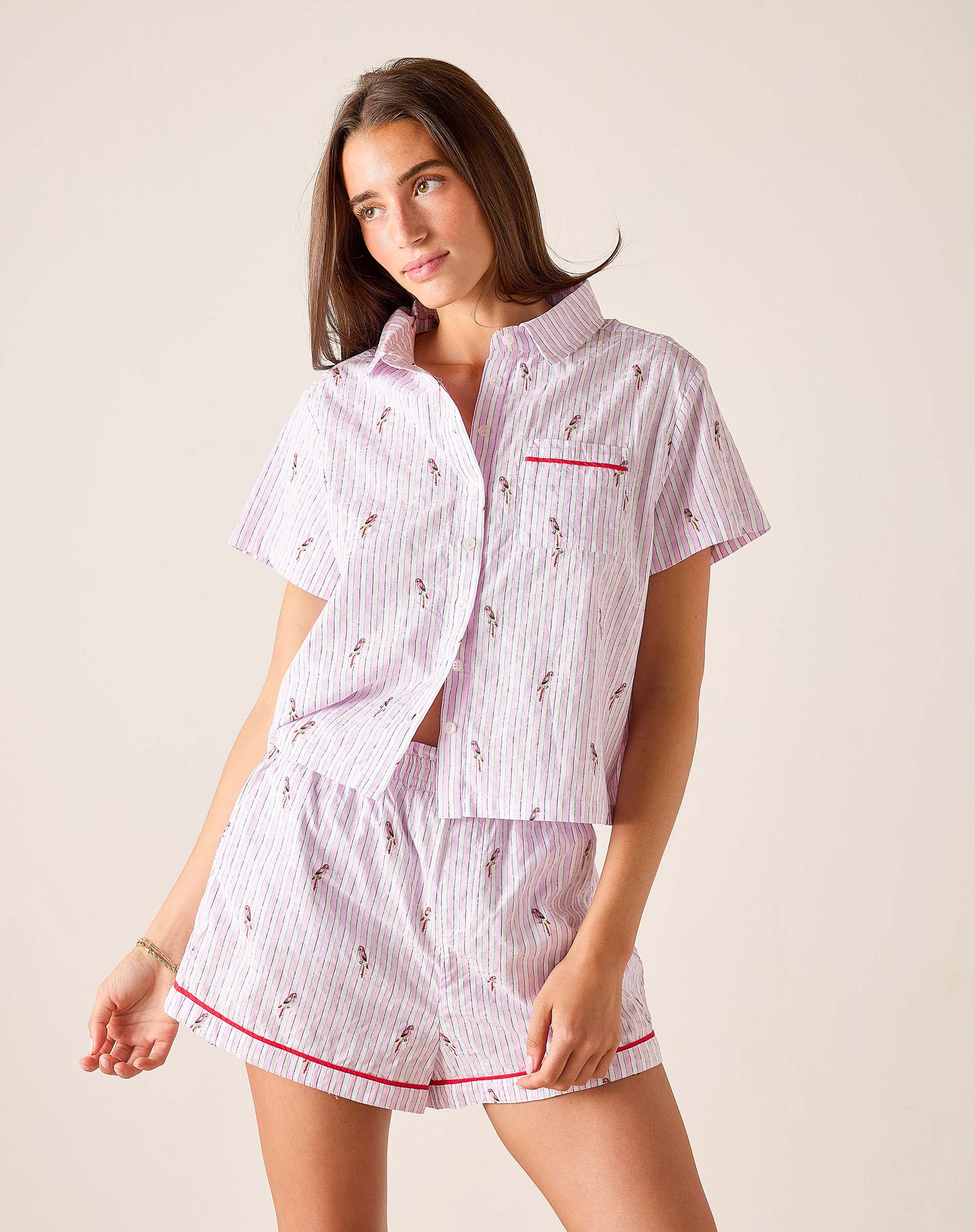 Woman wearing a pink and white striped pajama set with red accents on a beige background