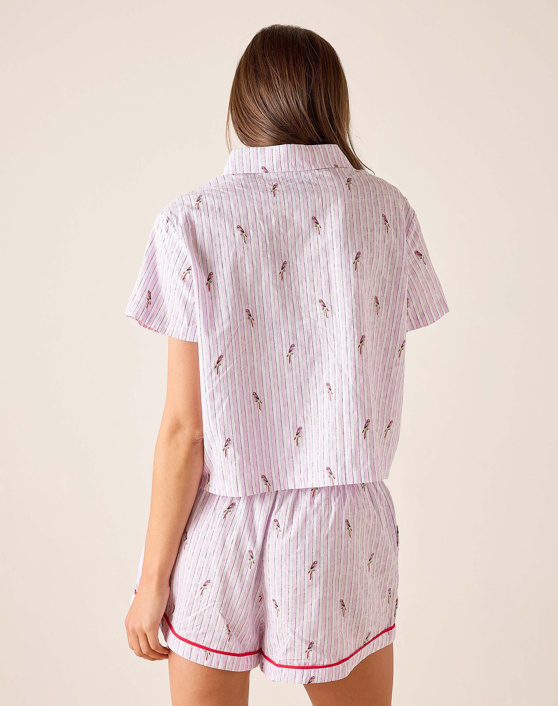 Woman wearing a pink and white striped pajama set with a subtle pattern on a beige background