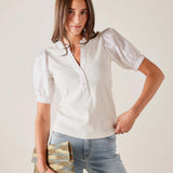 Woman wearing a white blouse and blue jeans, holding a woven clutch against a plain background