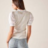 Woman wearing a light-colored blouse with puffed sleeves and light blue jeans against a plain background