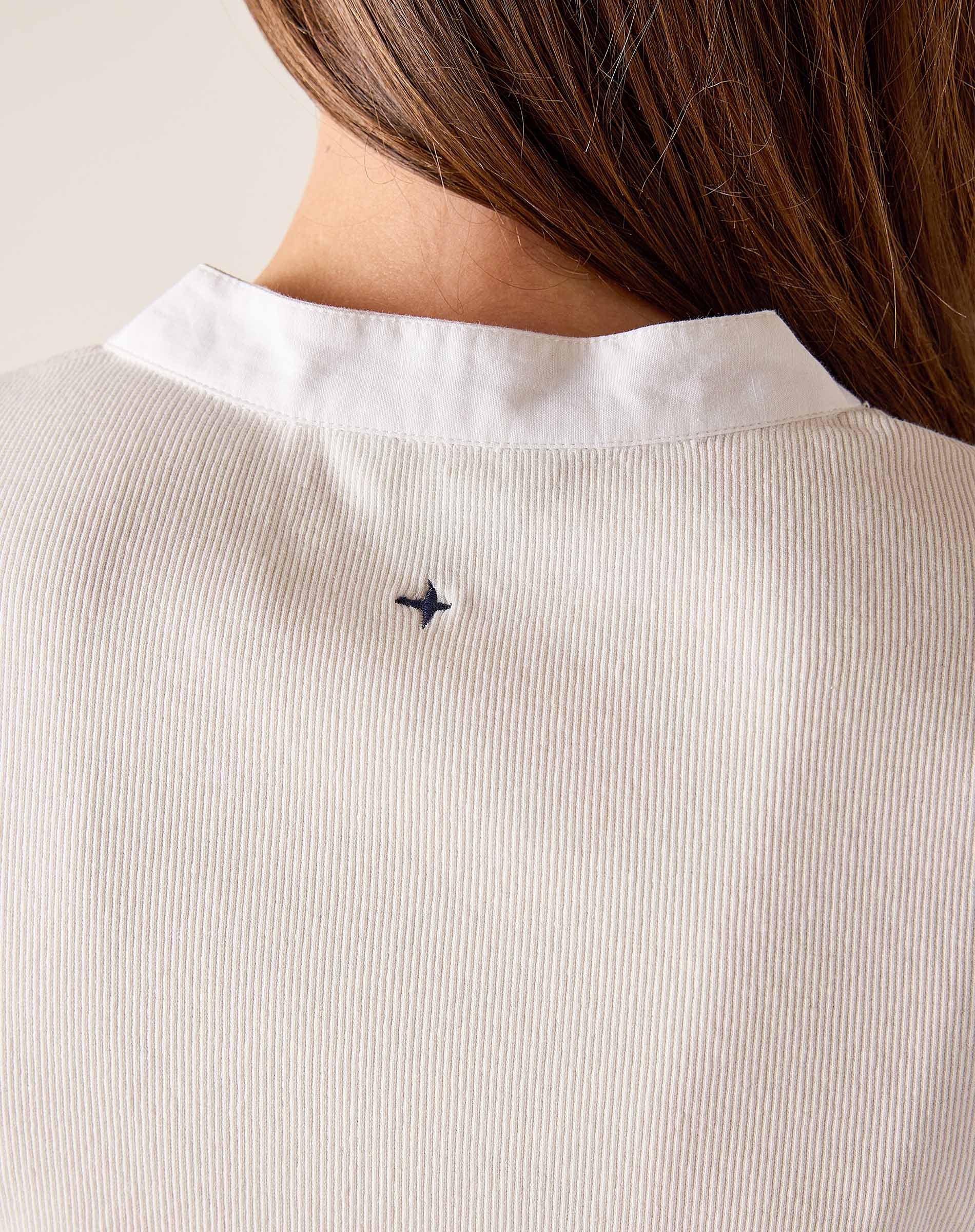 Close-up of a person wearing a white shirt with a small black logo on a light background