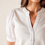 Close-up of a person wearing a white blouse with short sleeves and a necklace.