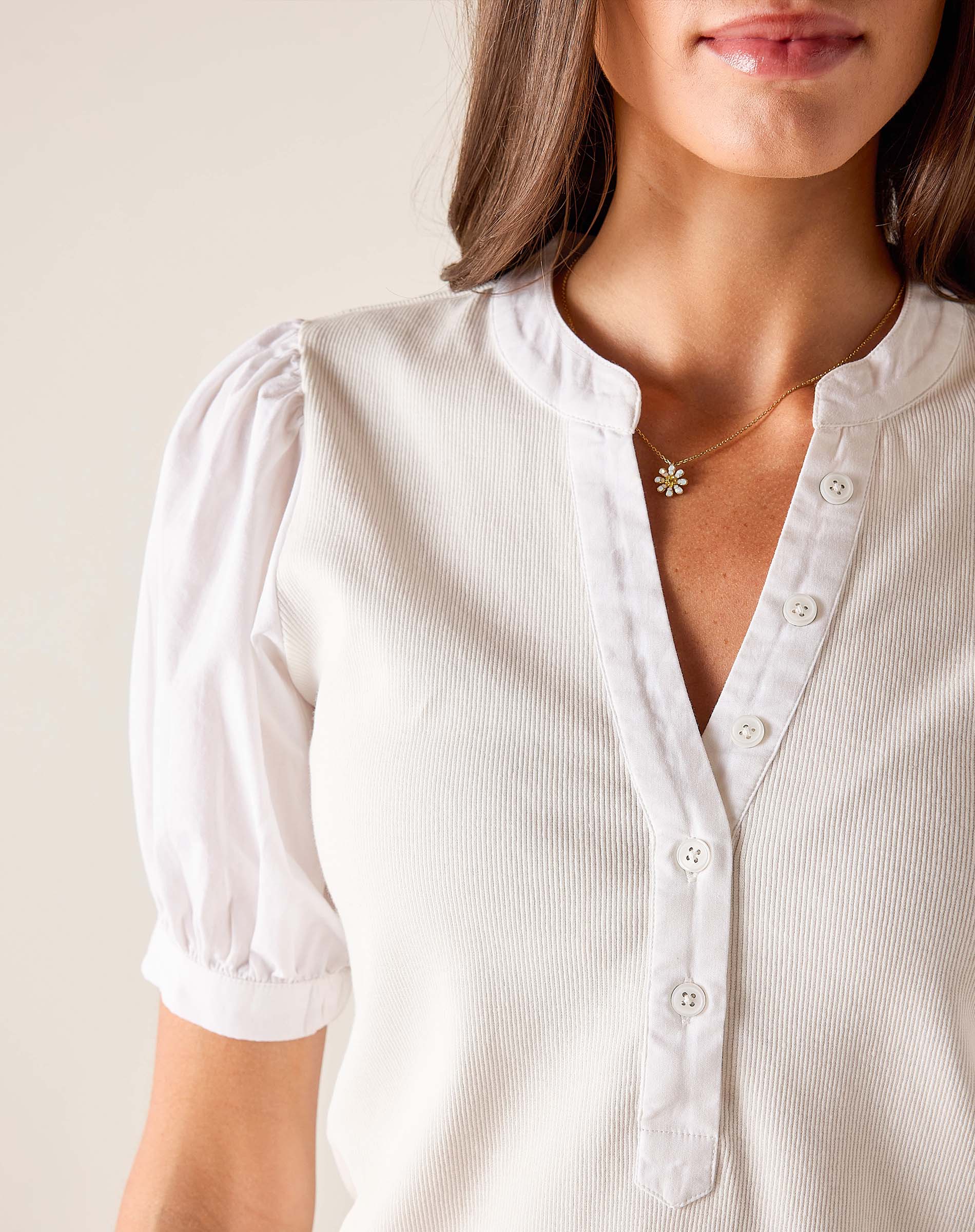 Close-up of a person wearing a white blouse with short sleeves and a necklace.