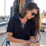 Woman sitting on a dock by a boat, wearing sunglasses and a navy shirt.