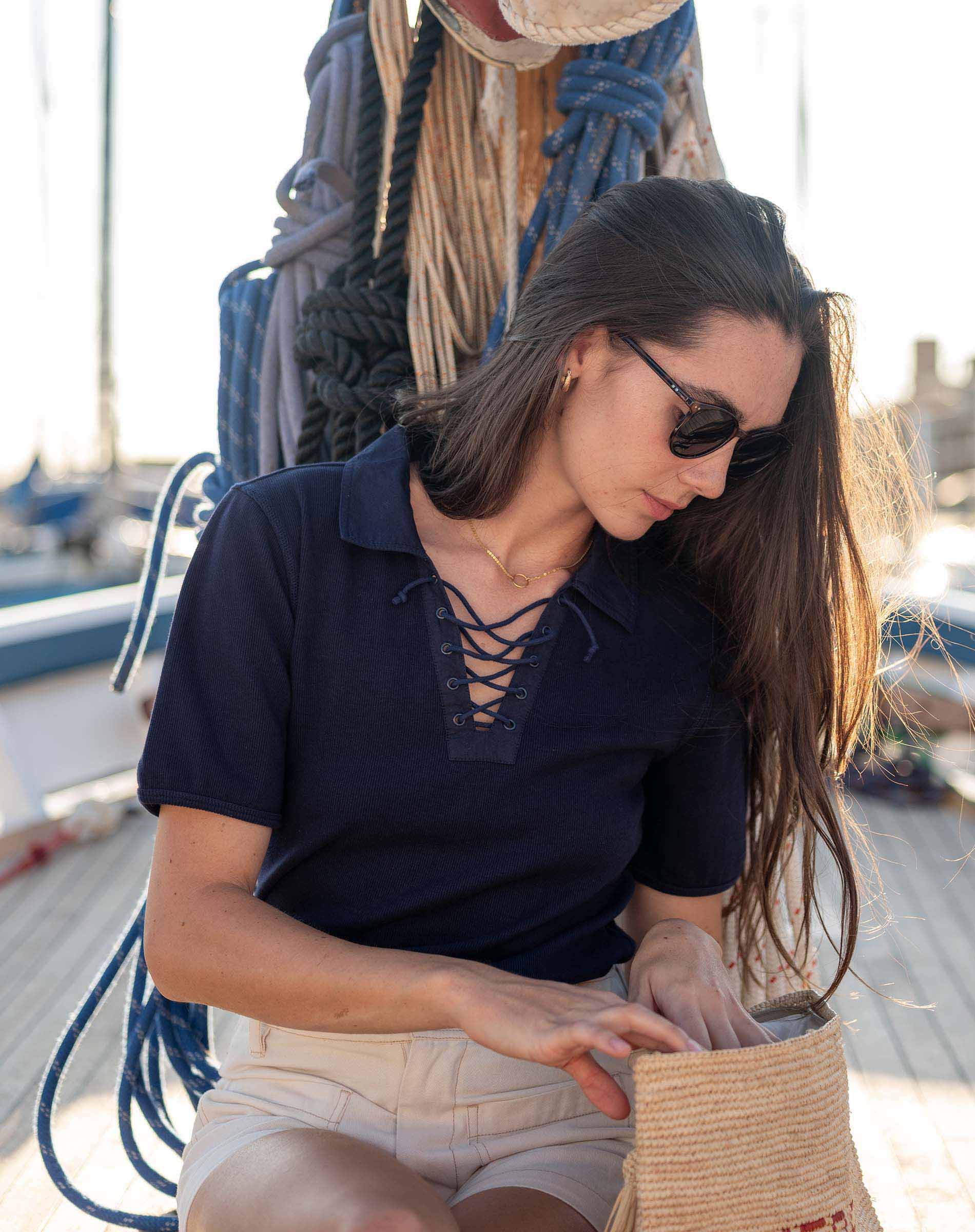 Woman sitting on a dock by a boat, wearing sunglasses and a navy shirt.