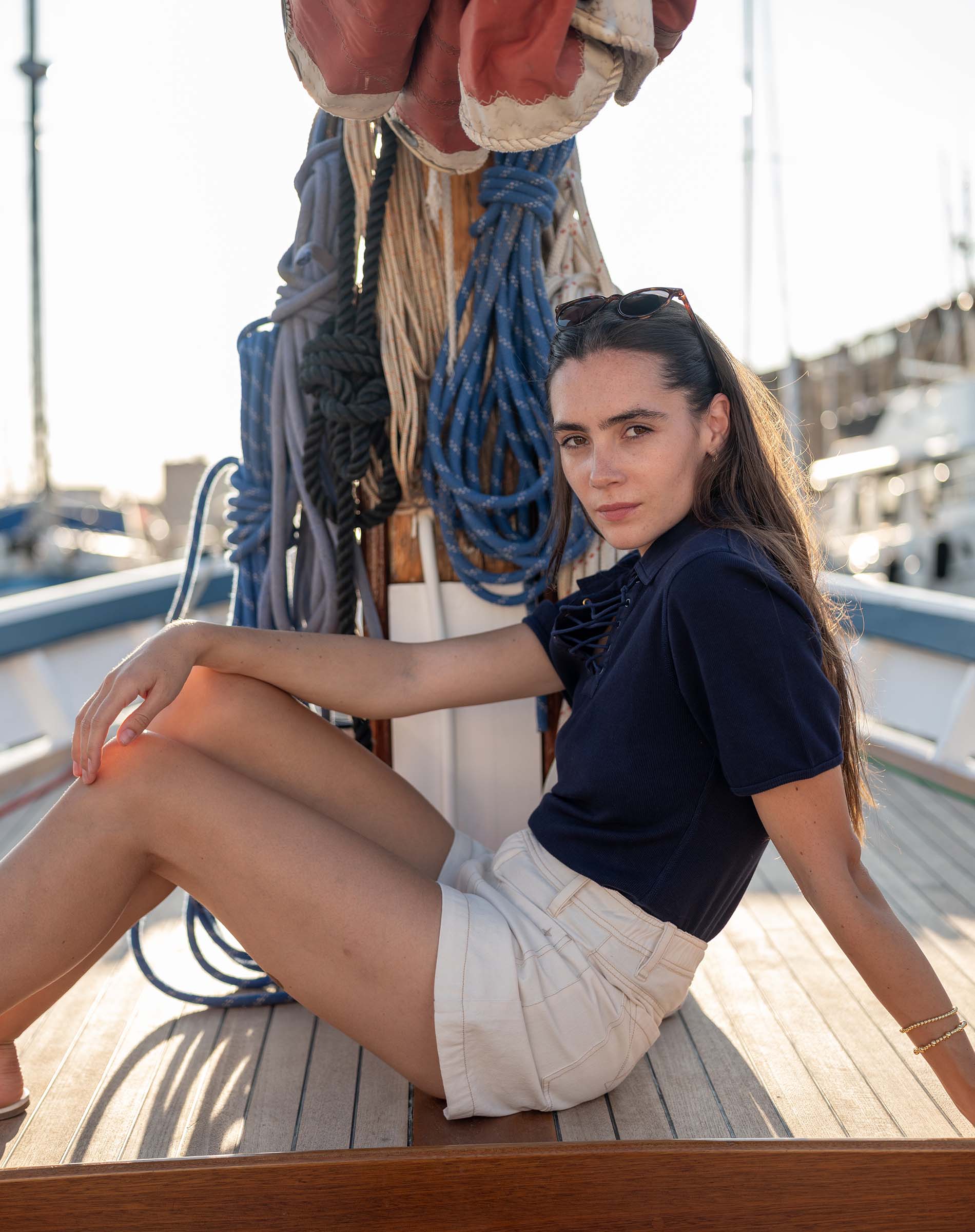 Woman sitting on a boat deck with ropes and nautical equipment in the background