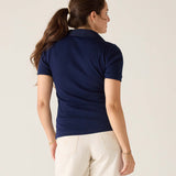 Woman wearing a navy blue polo shirt and white pants against a light background