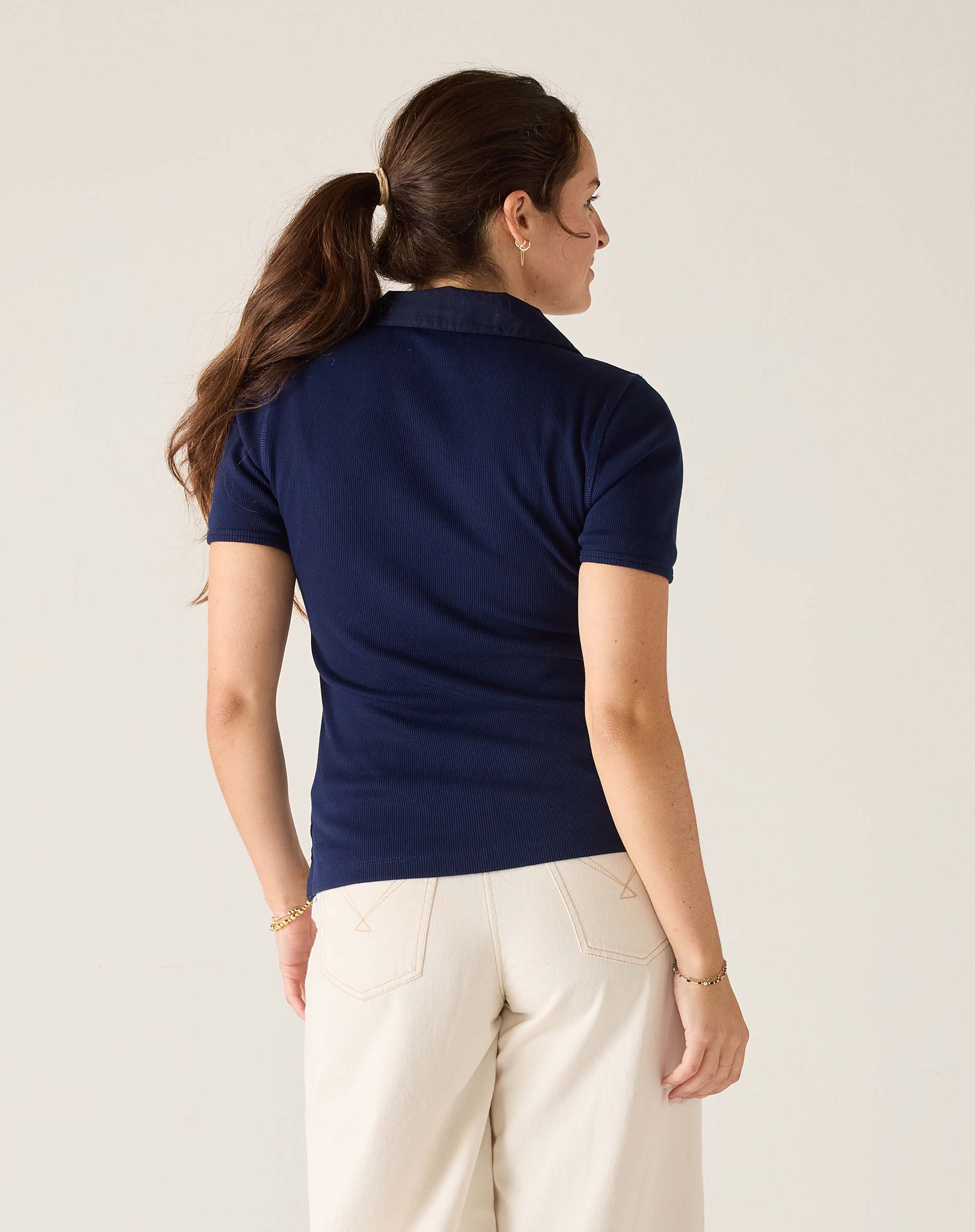 Woman wearing a navy blue polo shirt and white pants against a light background