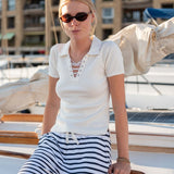 Woman in a white top and striped pants sitting on a boat with a marina background