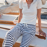Woman sitting on a boat wearing a white polo shirt and black and white striped pants.