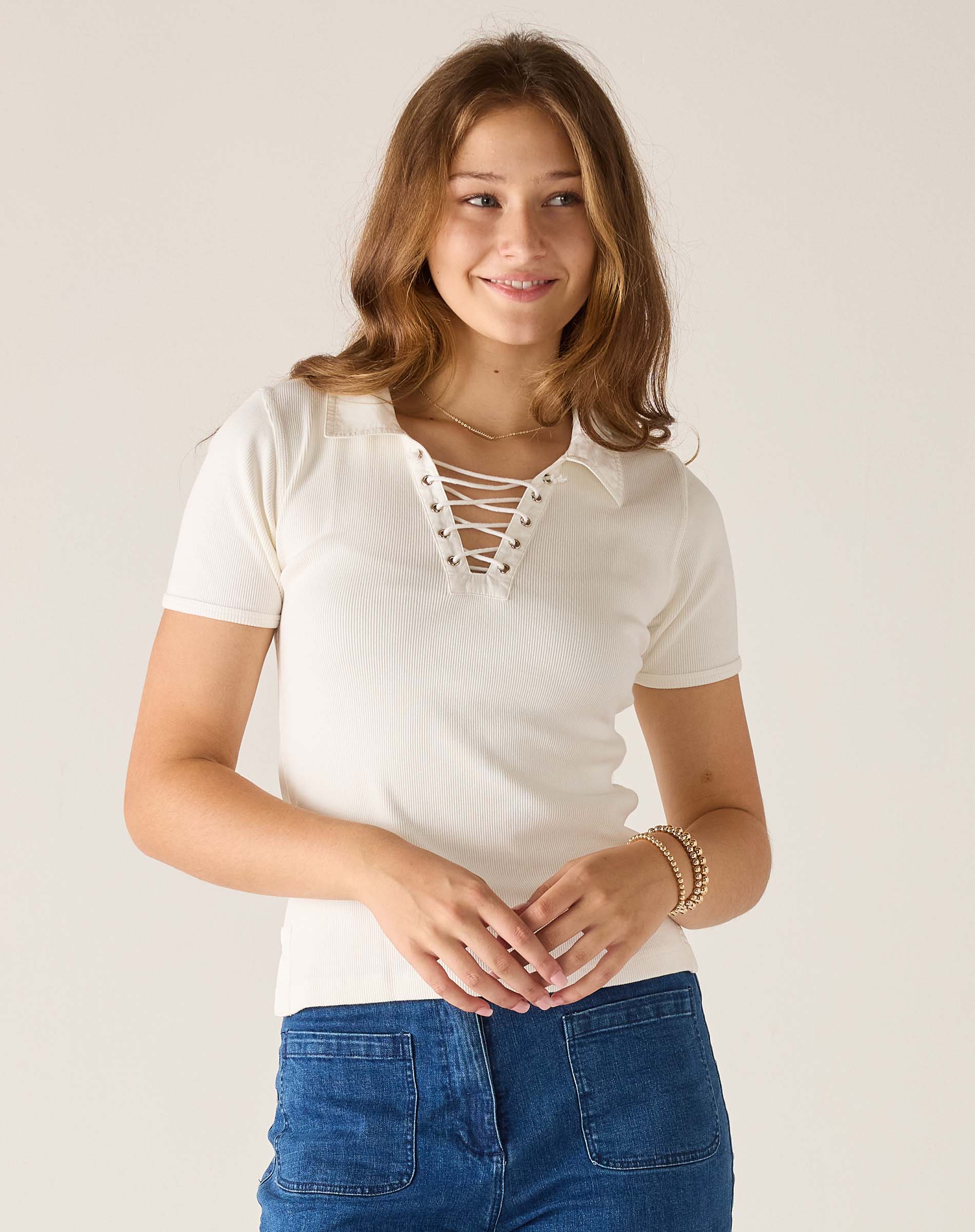 Woman wearing a white lace-up top and blue jeans against a plain background