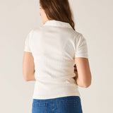 Person wearing a white polo shirt and blue jeans on a plain background