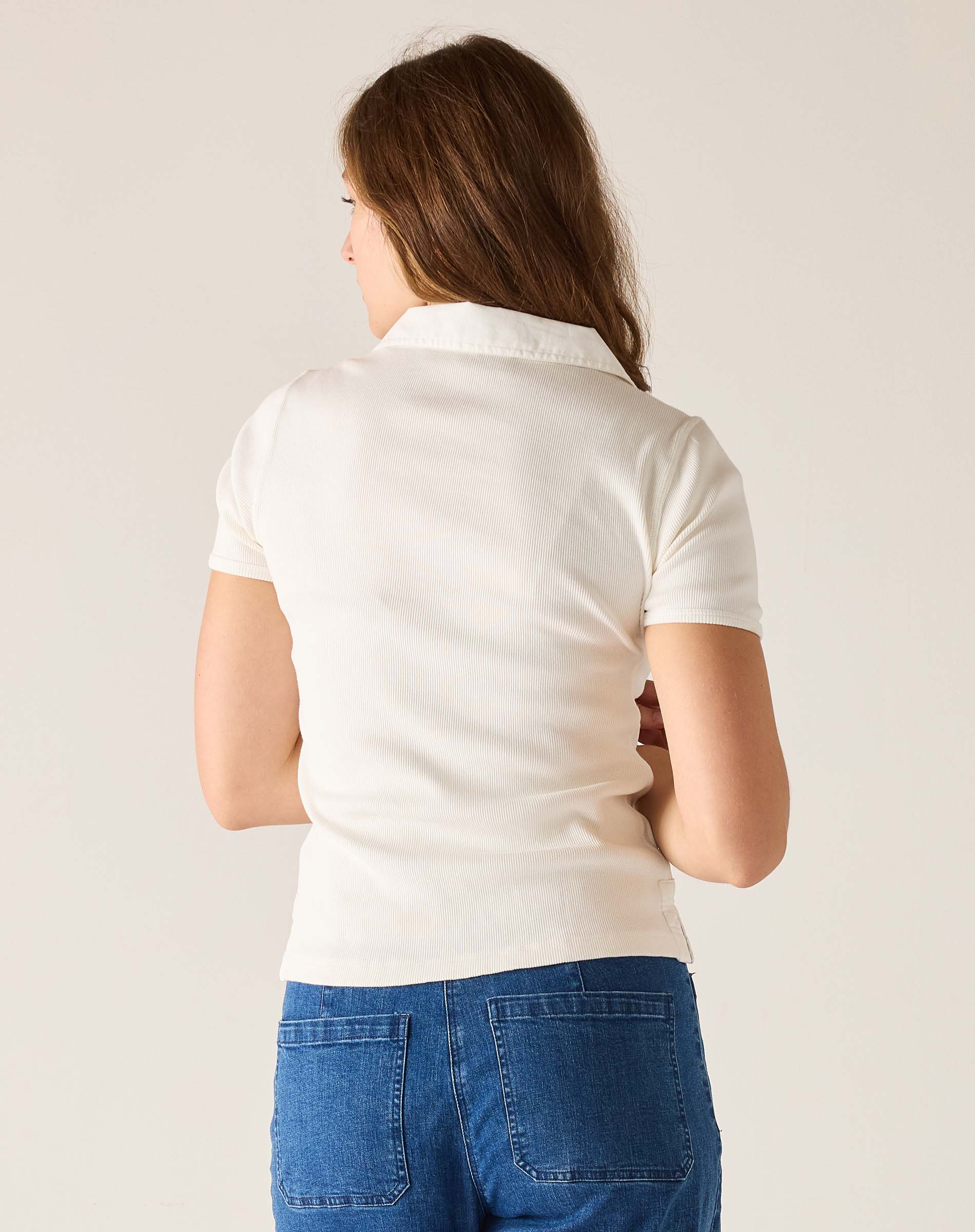Person wearing a white polo shirt and blue jeans on a plain background