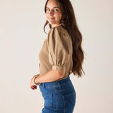 Woman wearing a beige blouse and blue denim skirt against a plain background