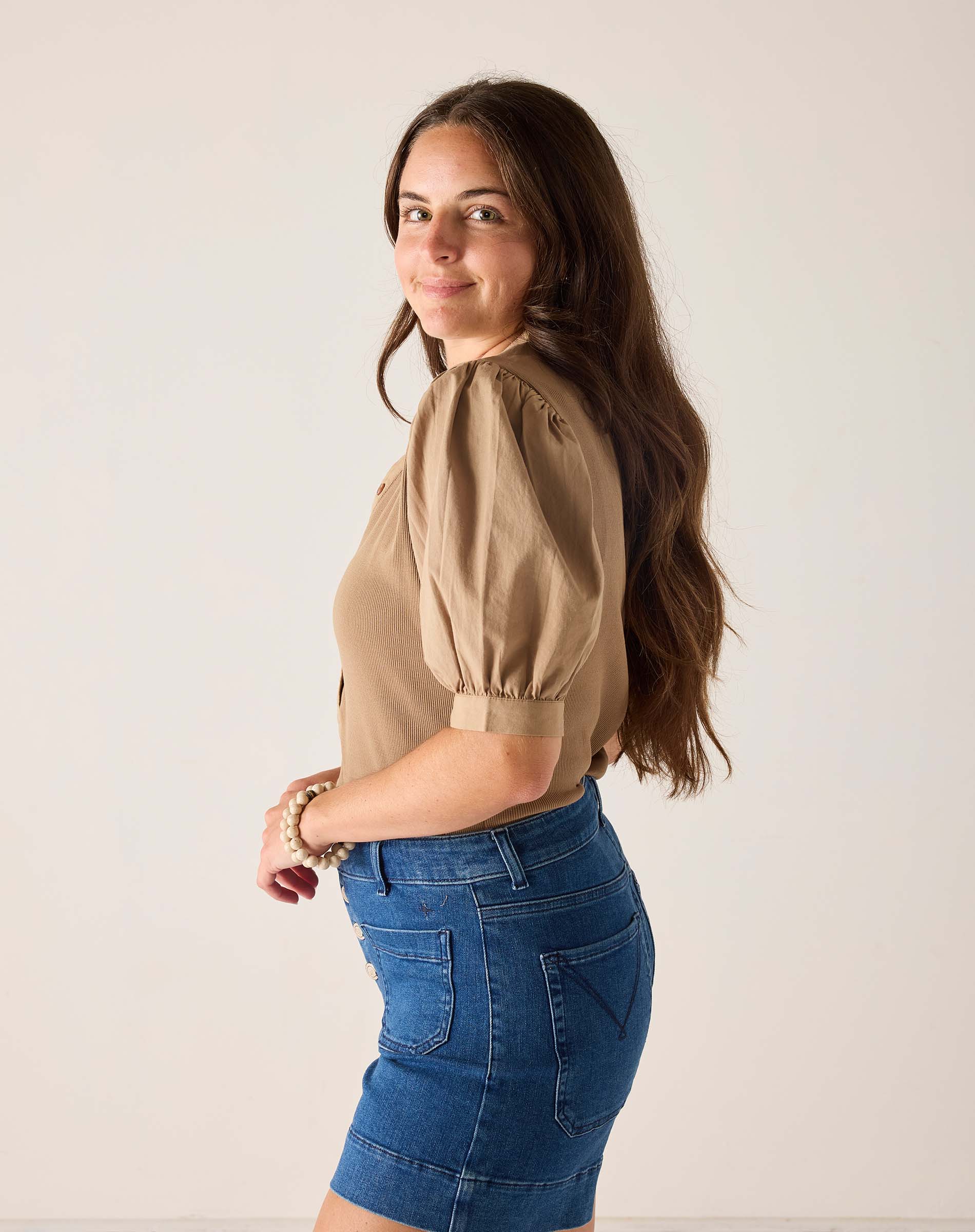 Woman wearing a beige blouse and blue denim skirt against a plain background