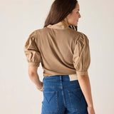 Woman wearing a beige blouse with puffed sleeves and blue denim shorts on a plain background