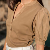 Woman wearing a brown blouse with short sleeves and a blurred background
