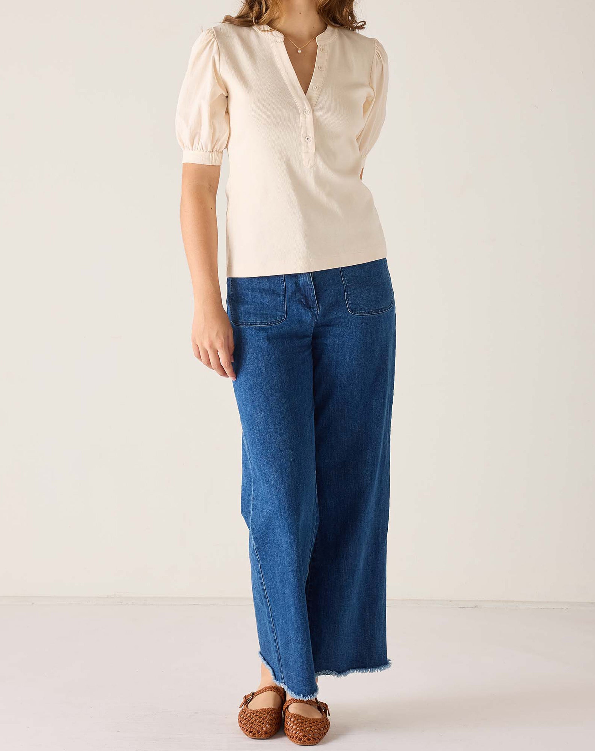 Person wearing a beige blouse and blue jeans on a white background