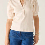 Person wearing a beige blouse with puffed sleeves and blue jeans on a plain background