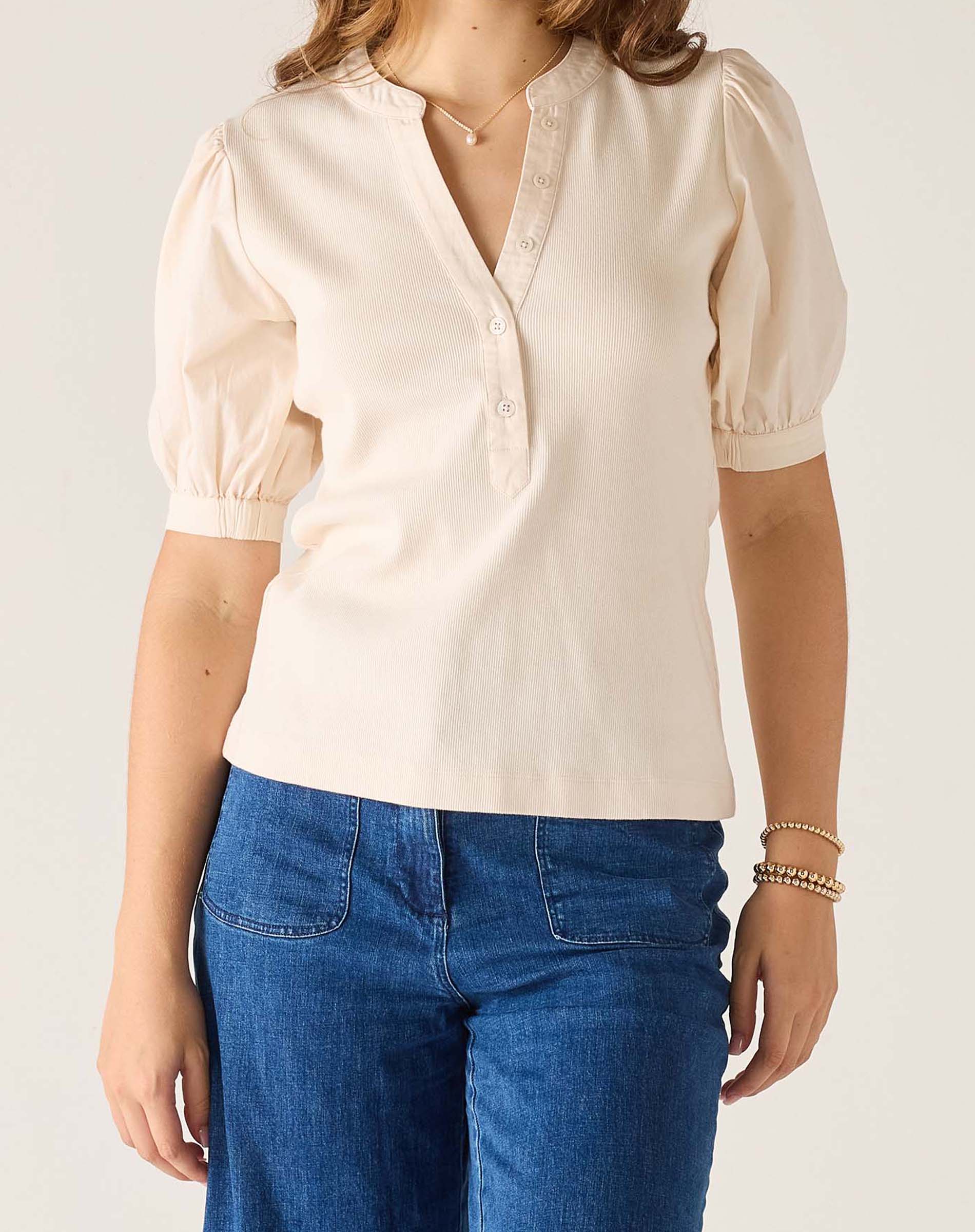 Person wearing a beige blouse with puffed sleeves and blue jeans on a plain background