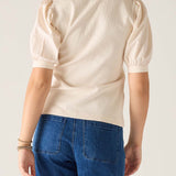 Person wearing a beige blouse with puffed sleeves and blue jeans on a plain background